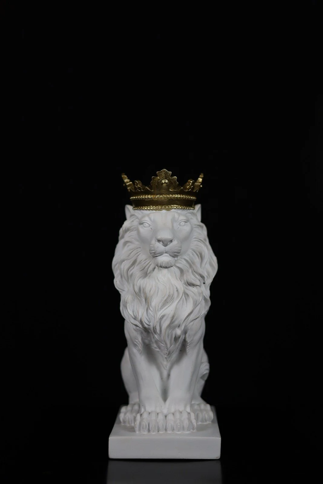 A white lion statue wearing a gold-colored crown against a black background.