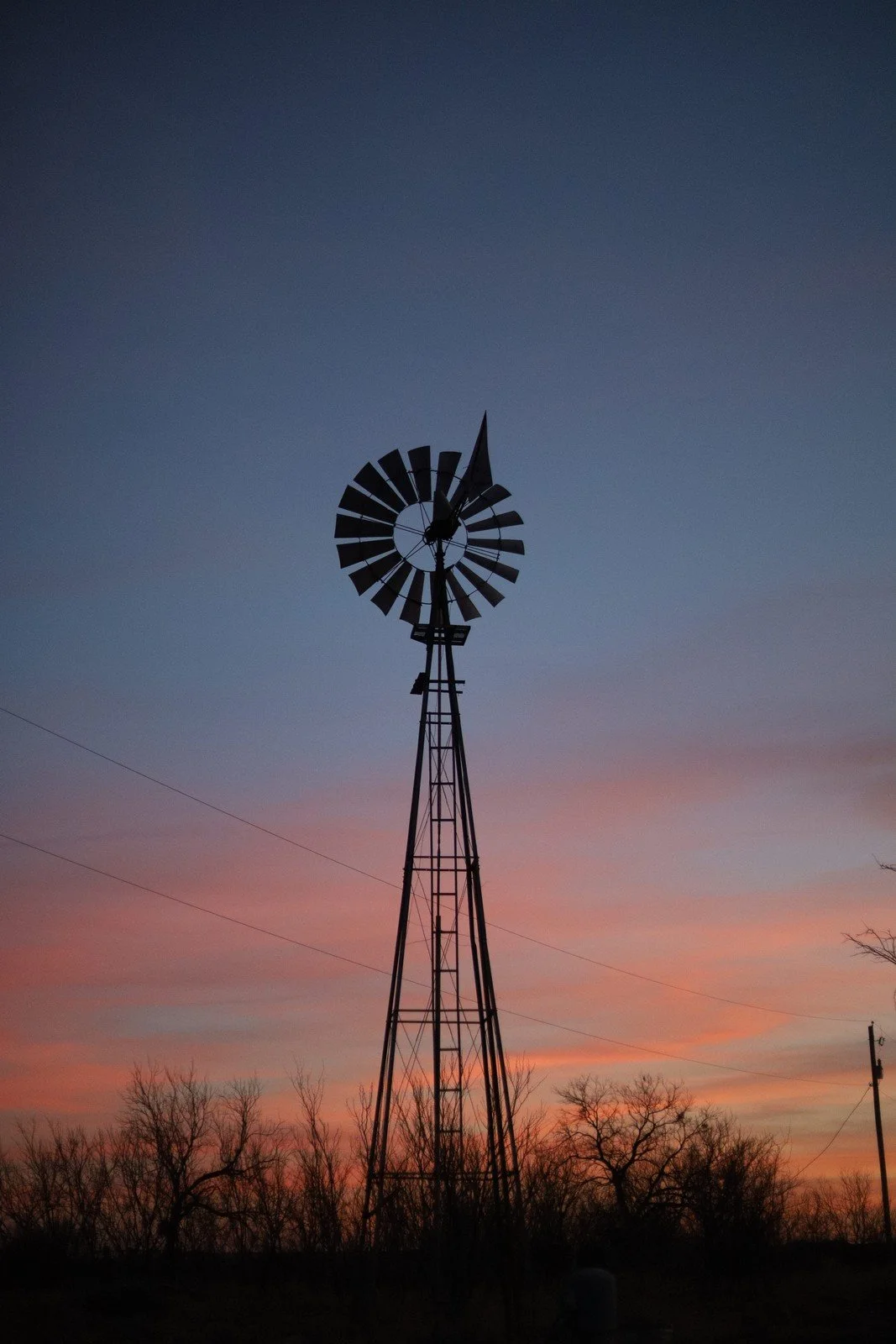 A silhouetted windmill beneath a blue and orange dusk sky.
