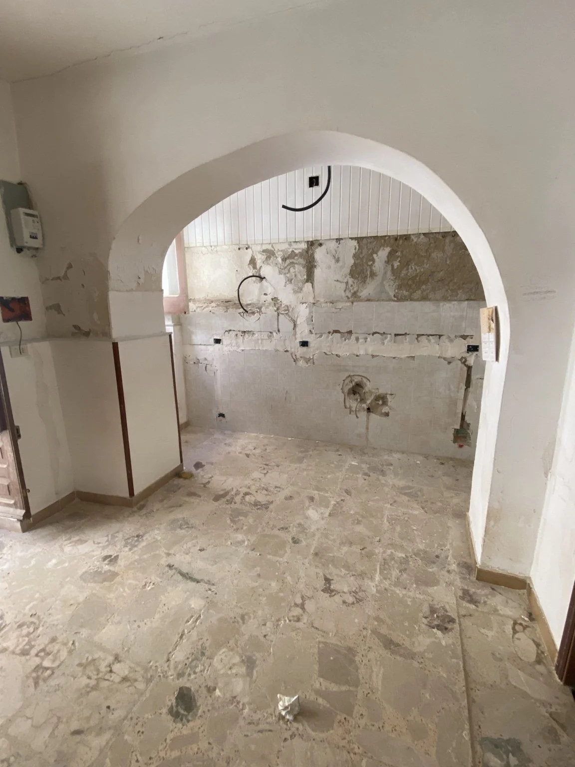 An arched opening, tiled walls, and exposed plaster.