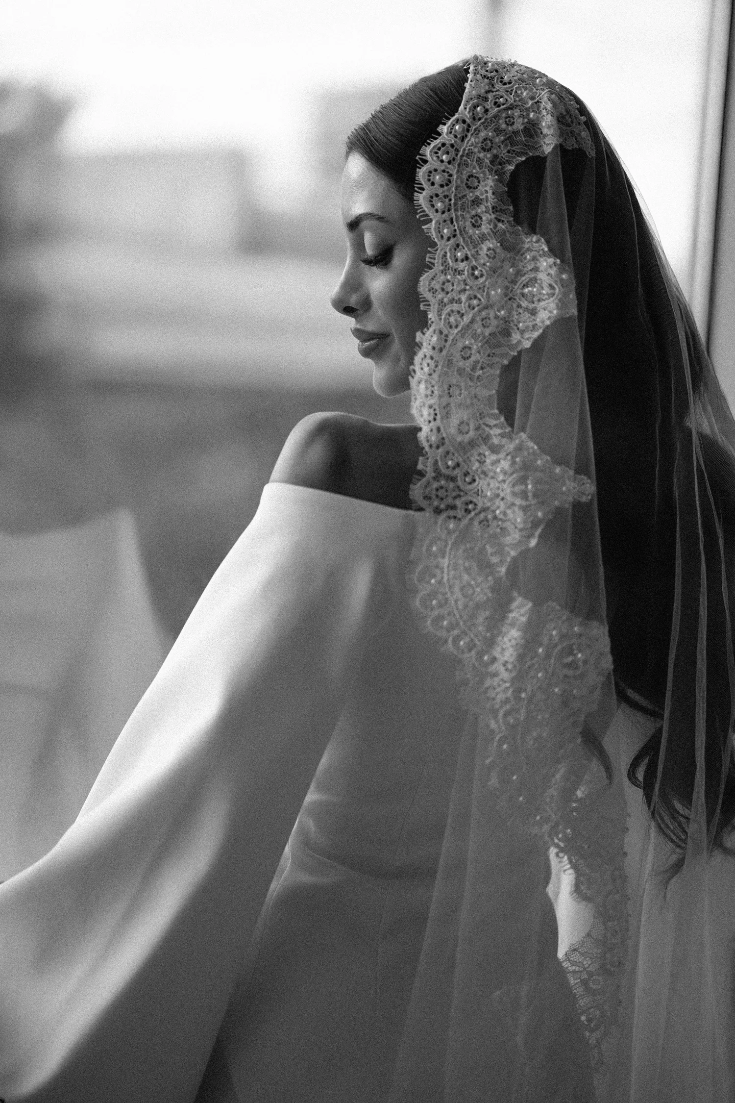 A bride in profile looks down, her lace edged veil falling over one shoulder