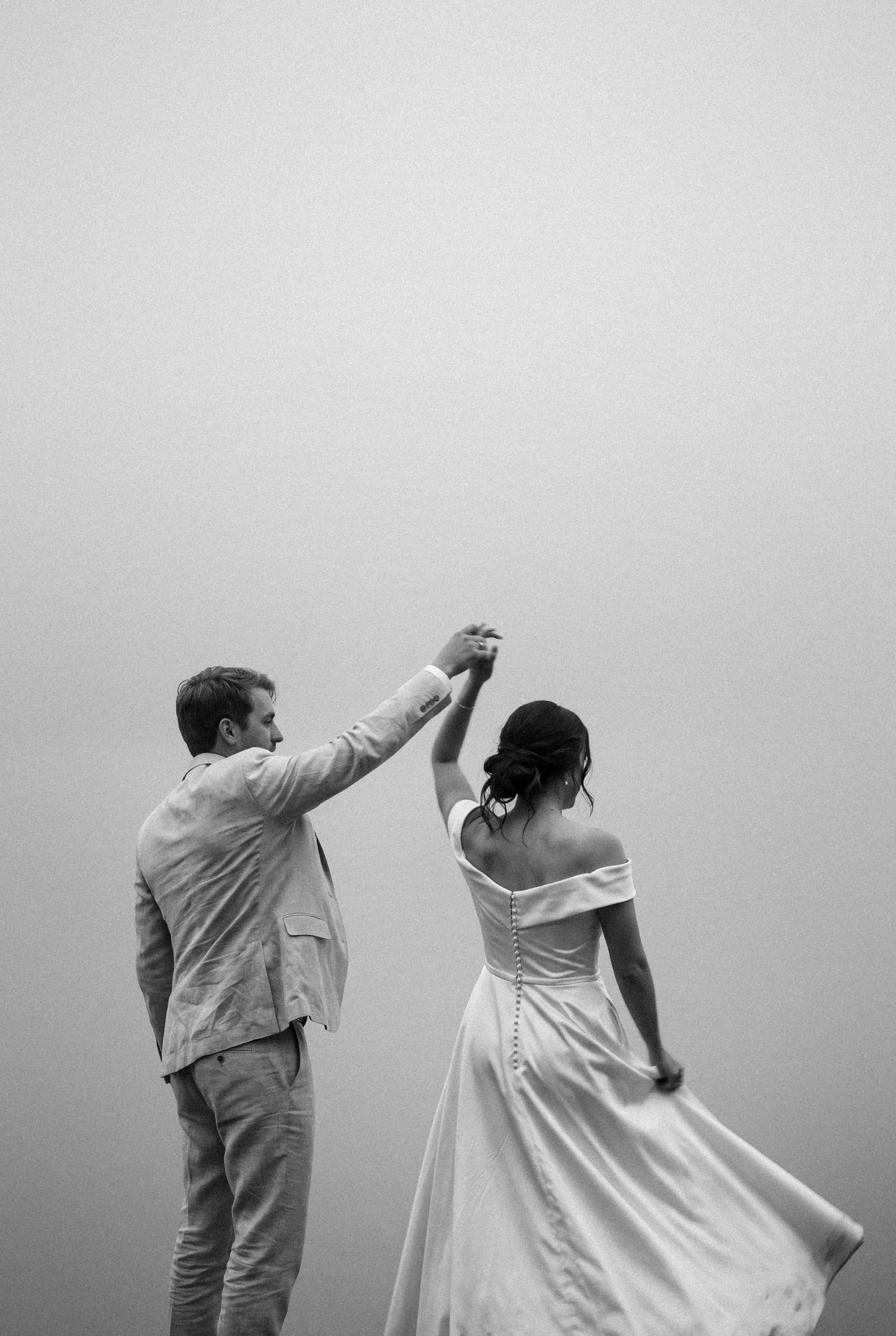 A groom twirls his bride in her flowing gown against a pale wall of mist