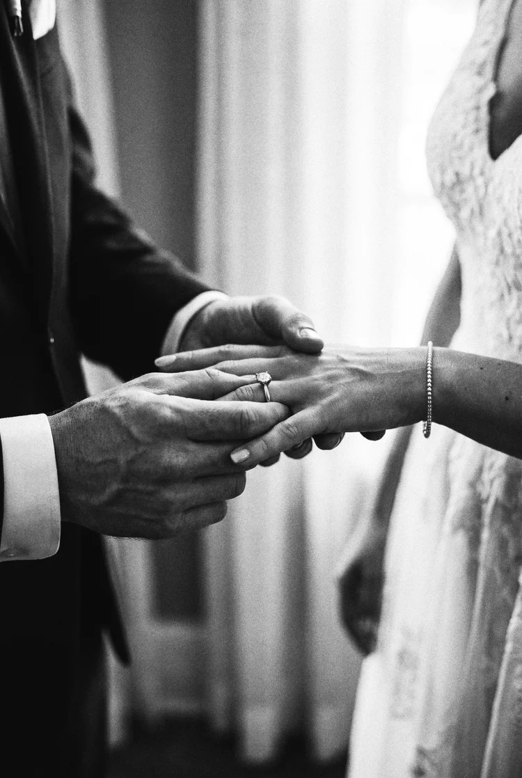 Close detail of a groom holding his bride by the hand, her diamond ring and bracelet catching the light