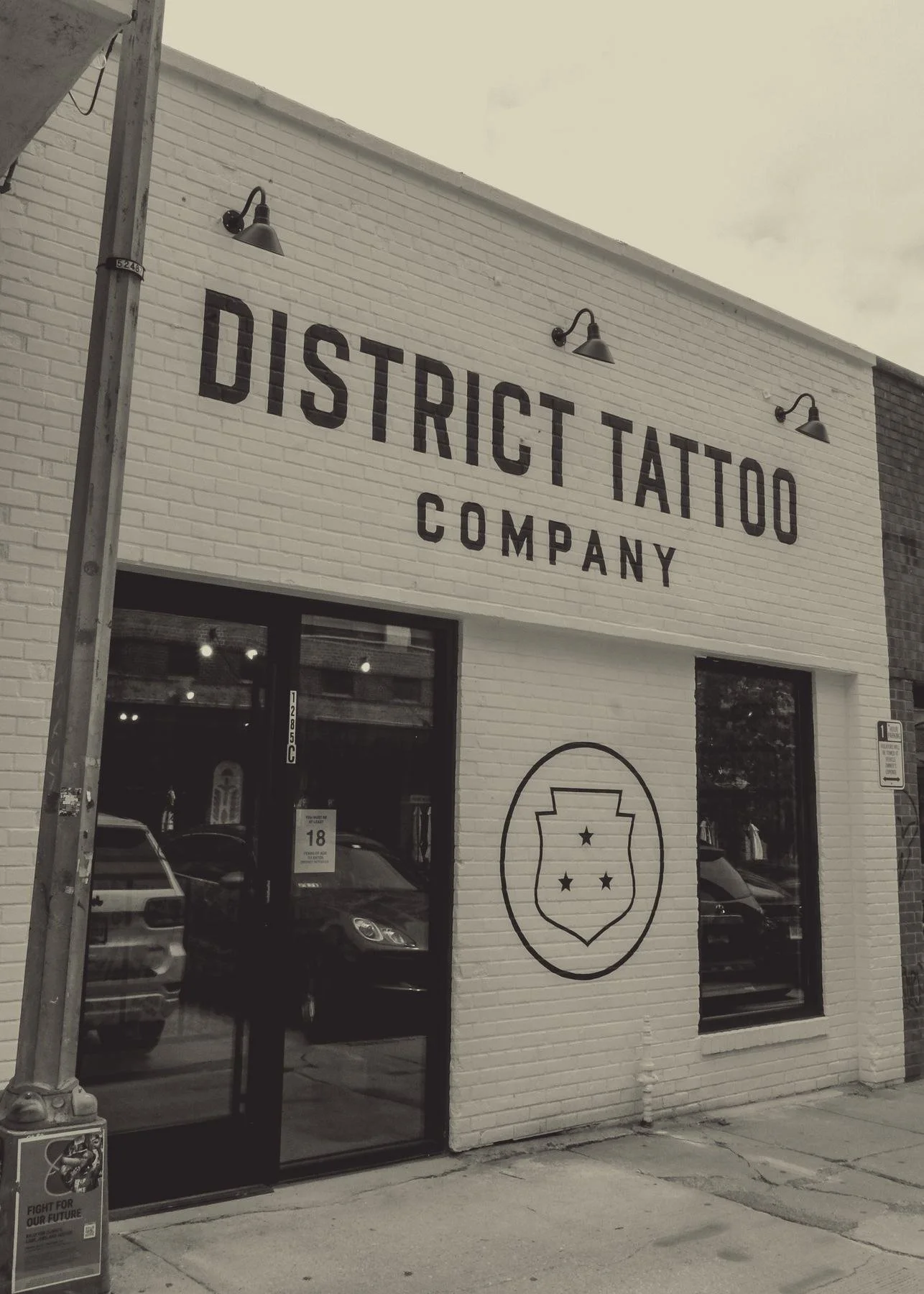 The District Tattoo Company storefront at 1285 4th St NE: white brick, the name painted above the door and the shield on the wall
