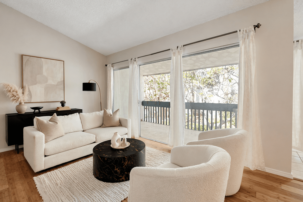 Living room with a sofa, two lounge chairs and sliding doors to the balcony, virtually staged