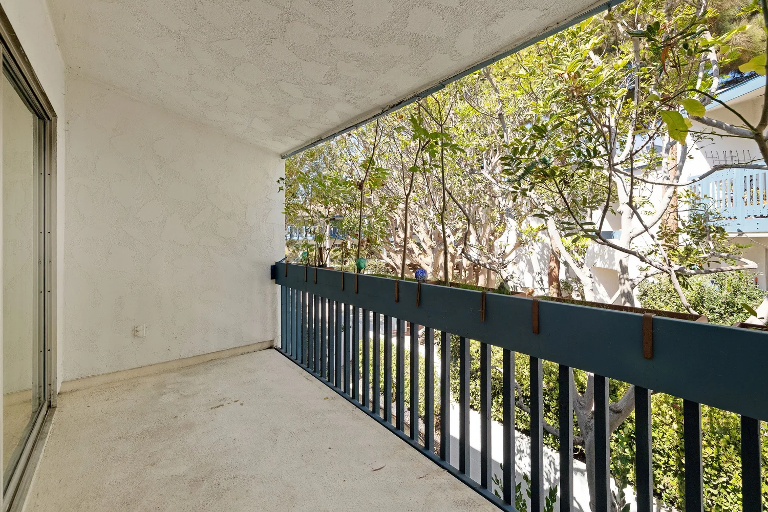 Covered balcony with a dark railing and trees beyond