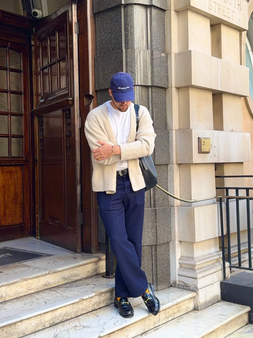Oskar in a cream cardigan, Abercrombie cap and navy trousers on stone steps, as posted by Abercrombie and Fitch