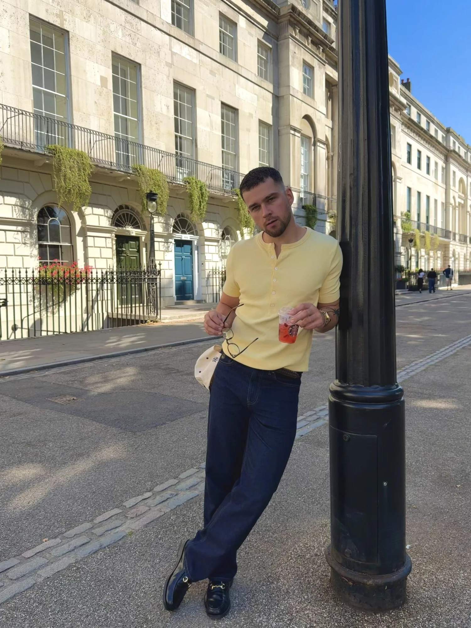 Oskar in a yellow henley and denim leaning on a lamp post