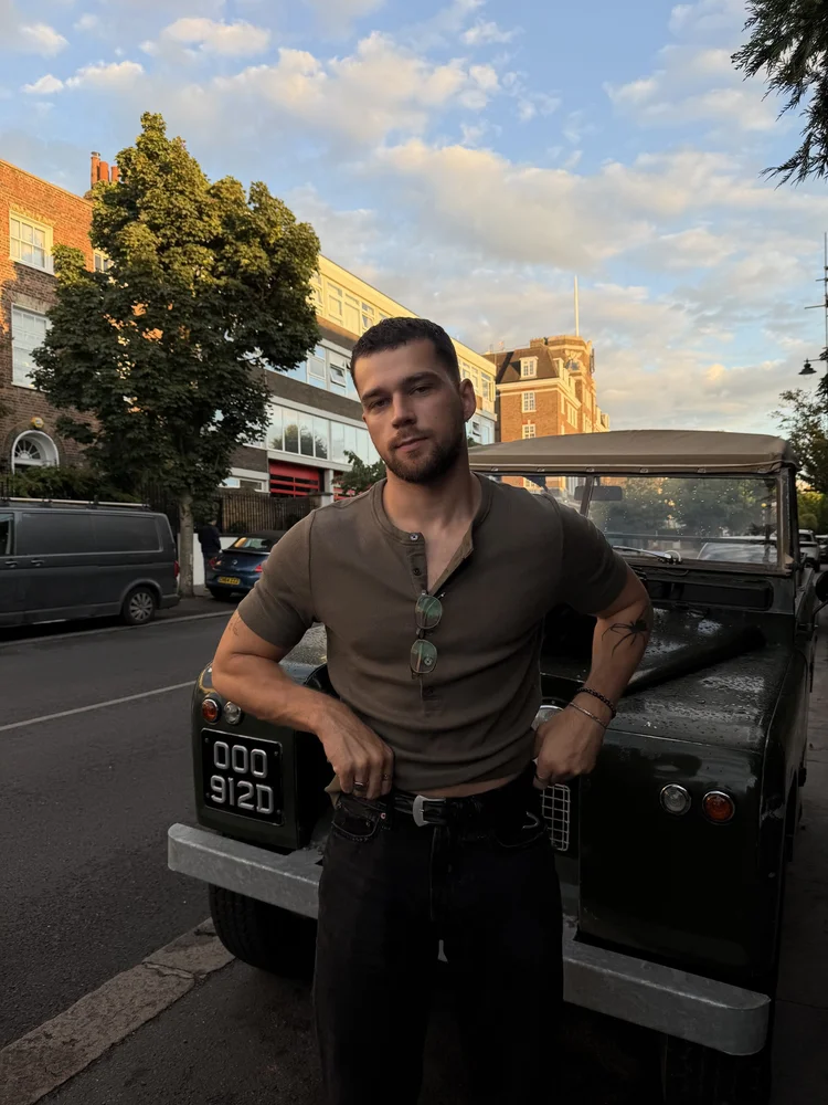 Olive henley leaning on a vintage Land Rover at sunset