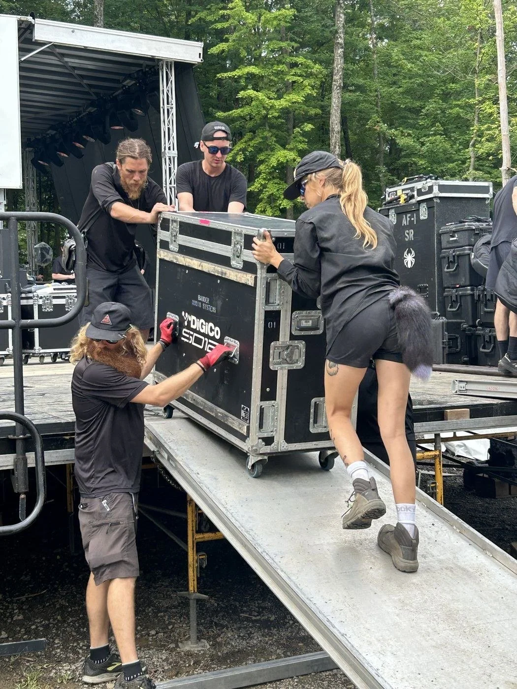 Four stagehands pushing a console road case up a ramp onto a festival stage