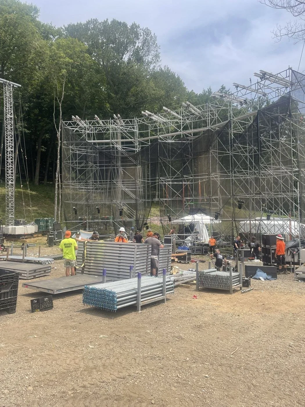 Stagehands building a scaffold stage in the woods, with stage deck and scaffold pipe staged on the ground
