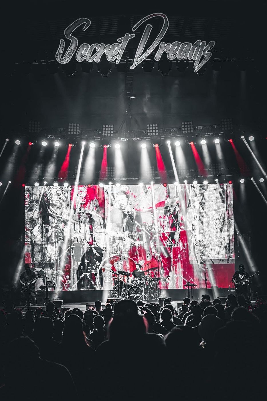 Band on a festival main stage under a lit Secret Dreams sign, with a large LED wall and beam lighting