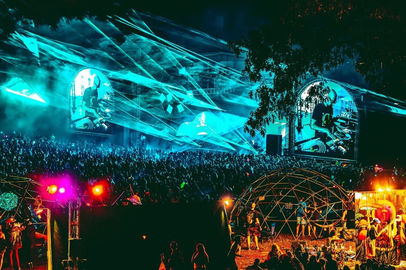 Laser and LED video show over a packed outdoor festival crowd at night, with arched video screens framing the stage