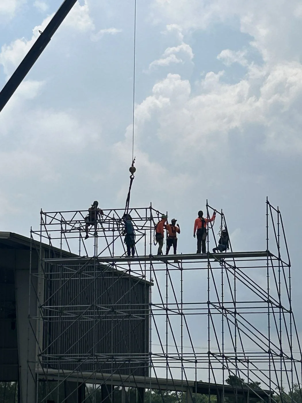 Riggers in fall-protection harnesses on top of a scaffold festival stage, guiding a crane pick