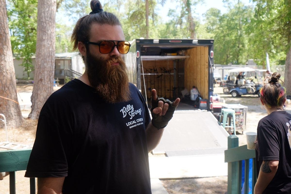 Crew member in a local crew shirt backstage beside an open equipment trailer