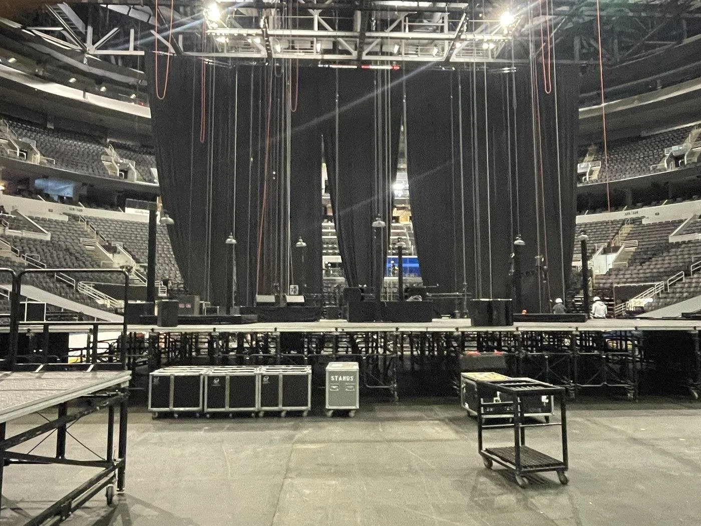 Arena stage build with black drape, chain hoists, monitor wedges and road cases during load-in