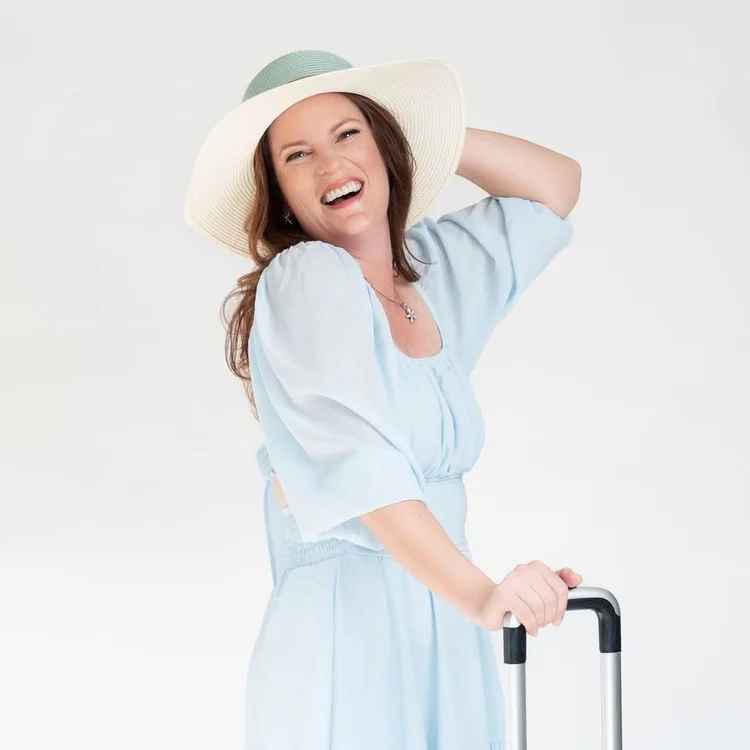 Samantha Robichaud laughing in a sun hat with a rolling suitcase