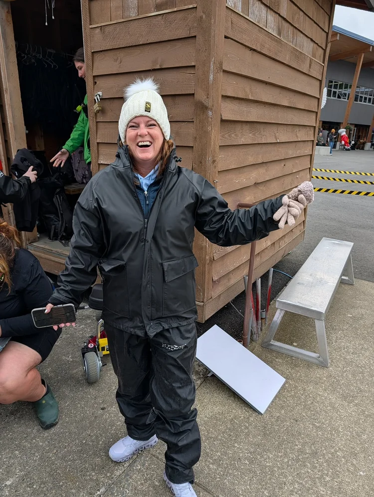 Samantha laughing, bundled up in rain gear and a white pom-pom hat