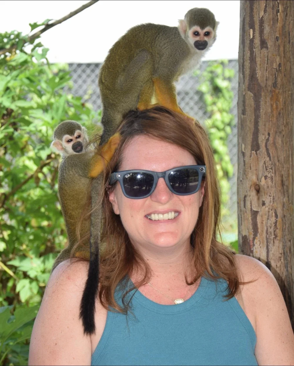 Samantha Robichaud smiling in sunglasses with two squirrel monkeys perched on her head and shoulder