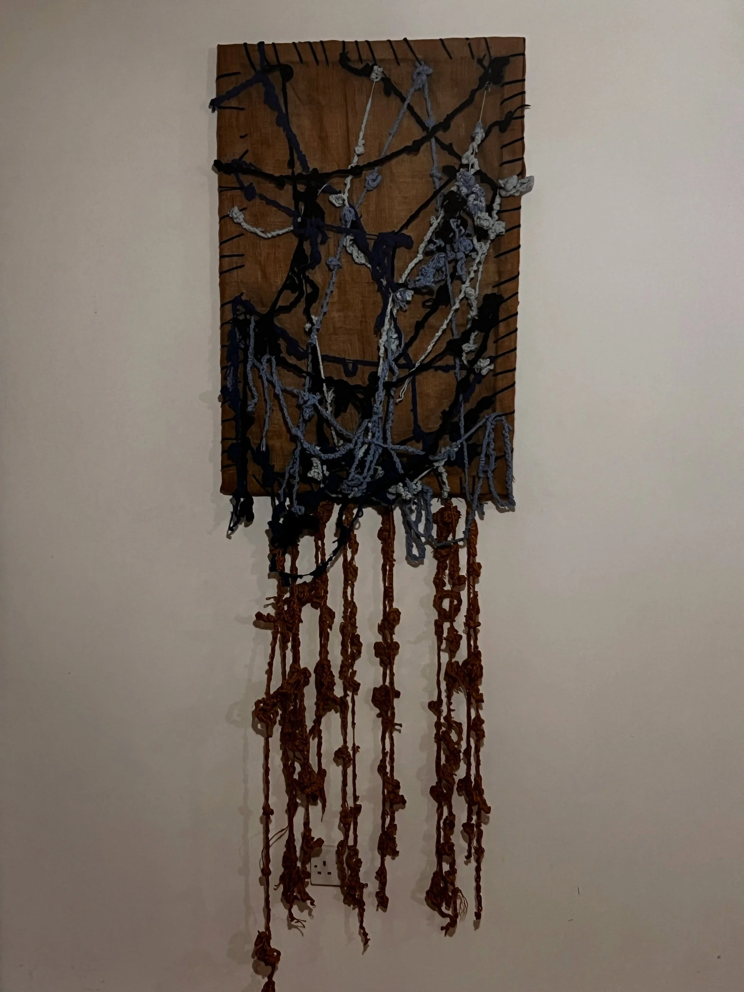 Su Taşkın’s hanging textile work with dark blue and grey threads and long knotted strands