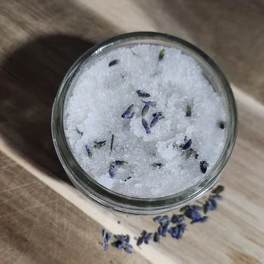 An open glass jar photographed from above on a wooden surface, with purple buds visible.