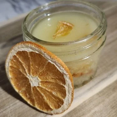 A close view of an open glass jar with a dried orange slice leaning against it.