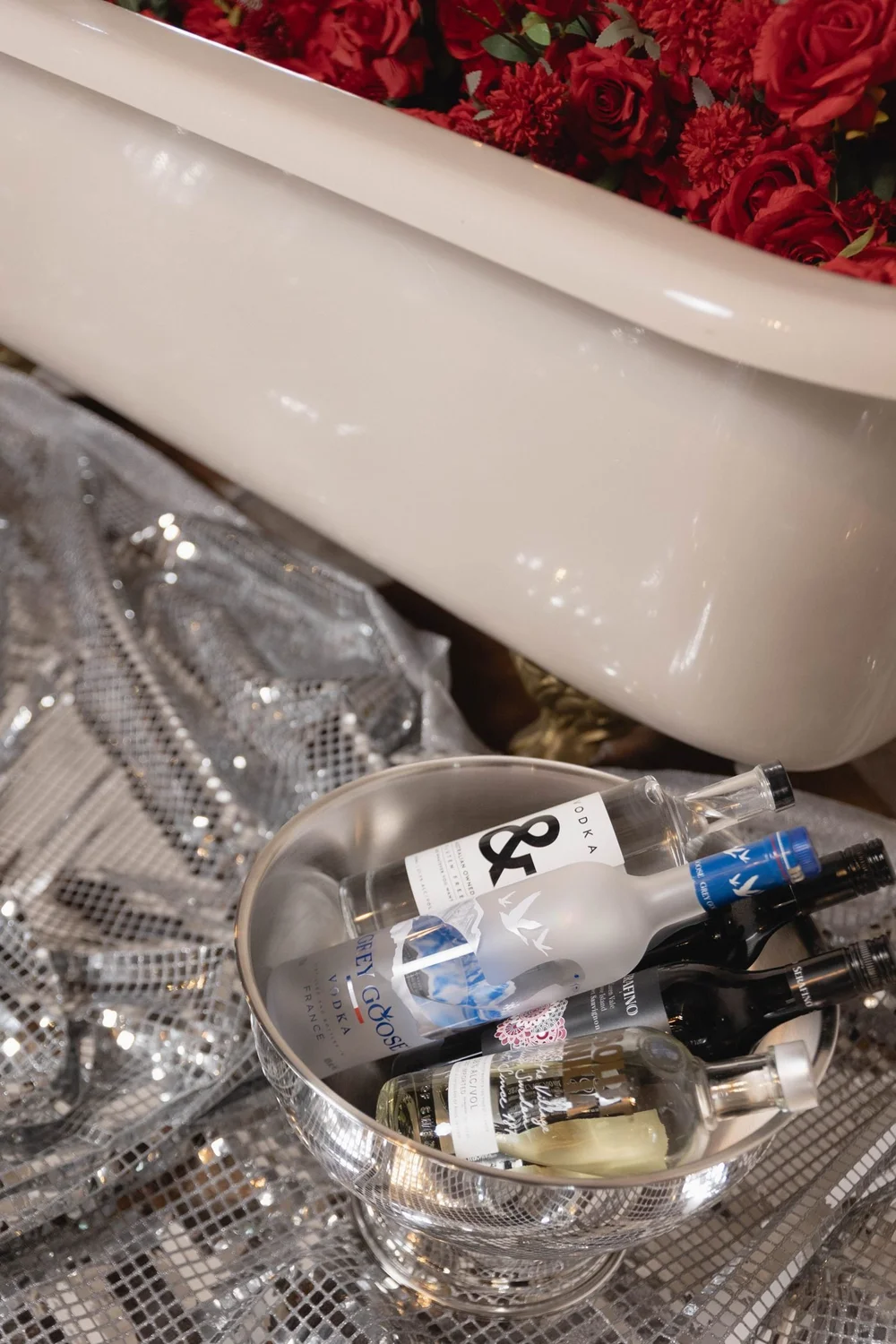 Silver ice bucket of drinks beside the rose-filled bath