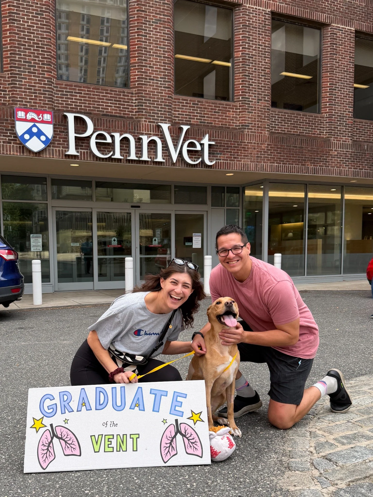 Noodle with his family outside Penn Vet, beside his Graduate of the Vent sign.