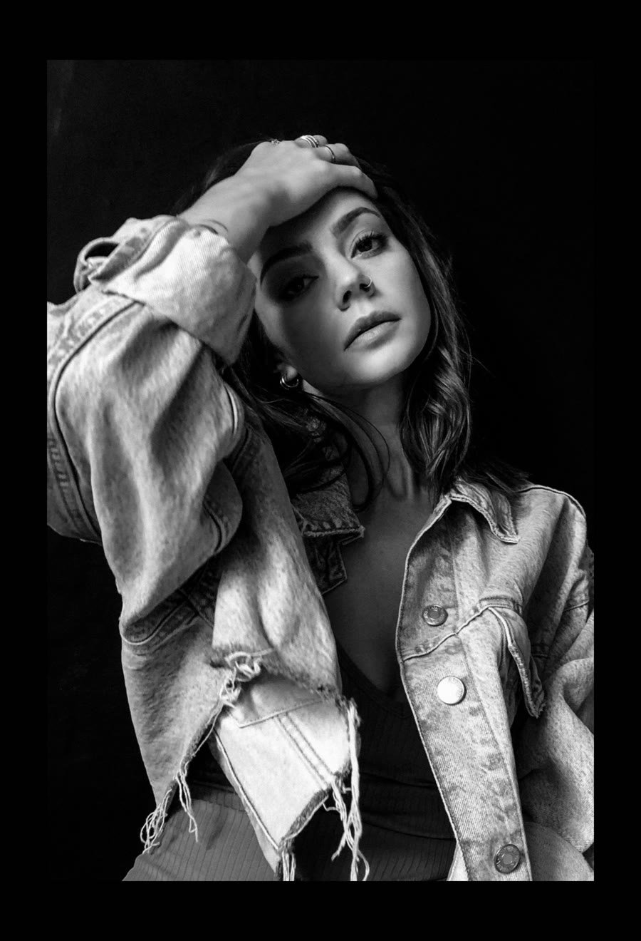 Black-and-white portrait of a dancer in a cropped denim jacket, one hand resting on her head.