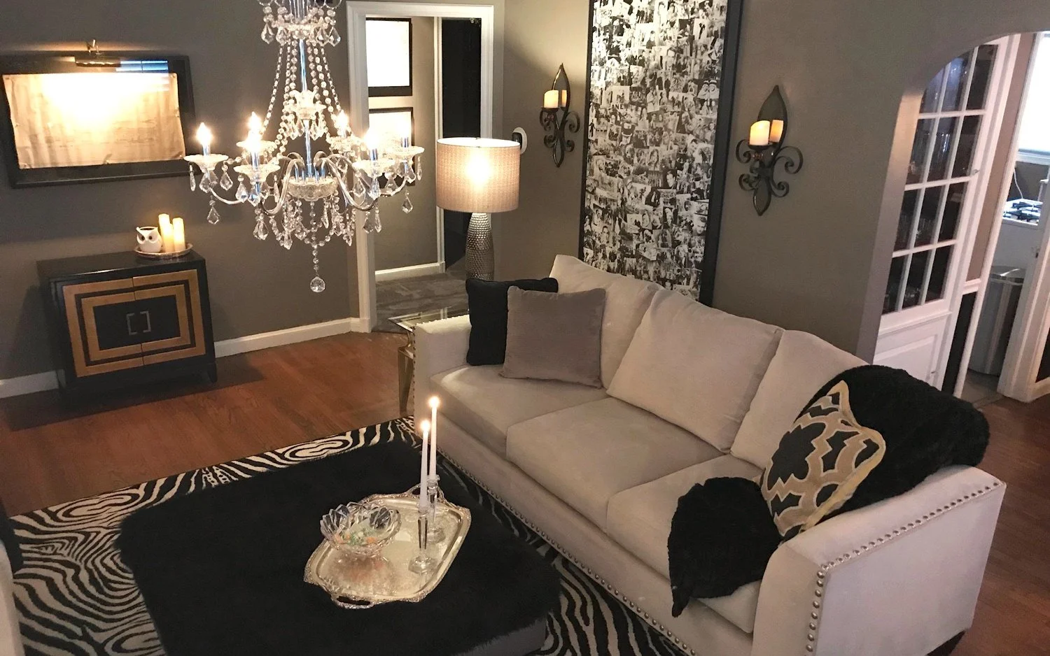 Living room by Morgan House of Design with crystal chandelier, cream nailhead sofa and black fur ottoman in warm lamp light
