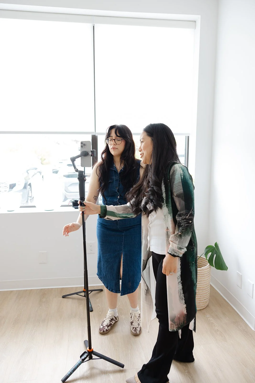 Two creators setting up a phone on a tripod to film by the studio's big window