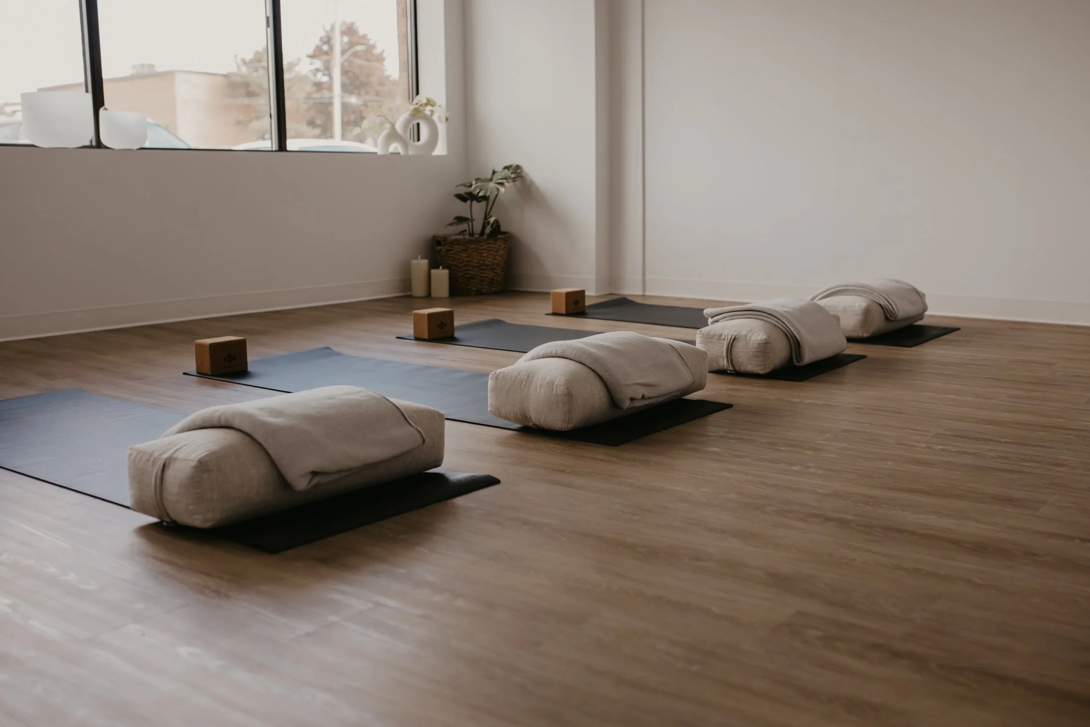 The bright studio room with wood floors, a wide window and yoga mats, bolsters and blocks set out
