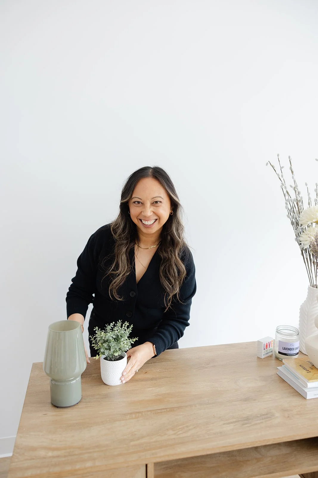 A smiling woman styling a plant on the studio's wooden desk during a branding shoot