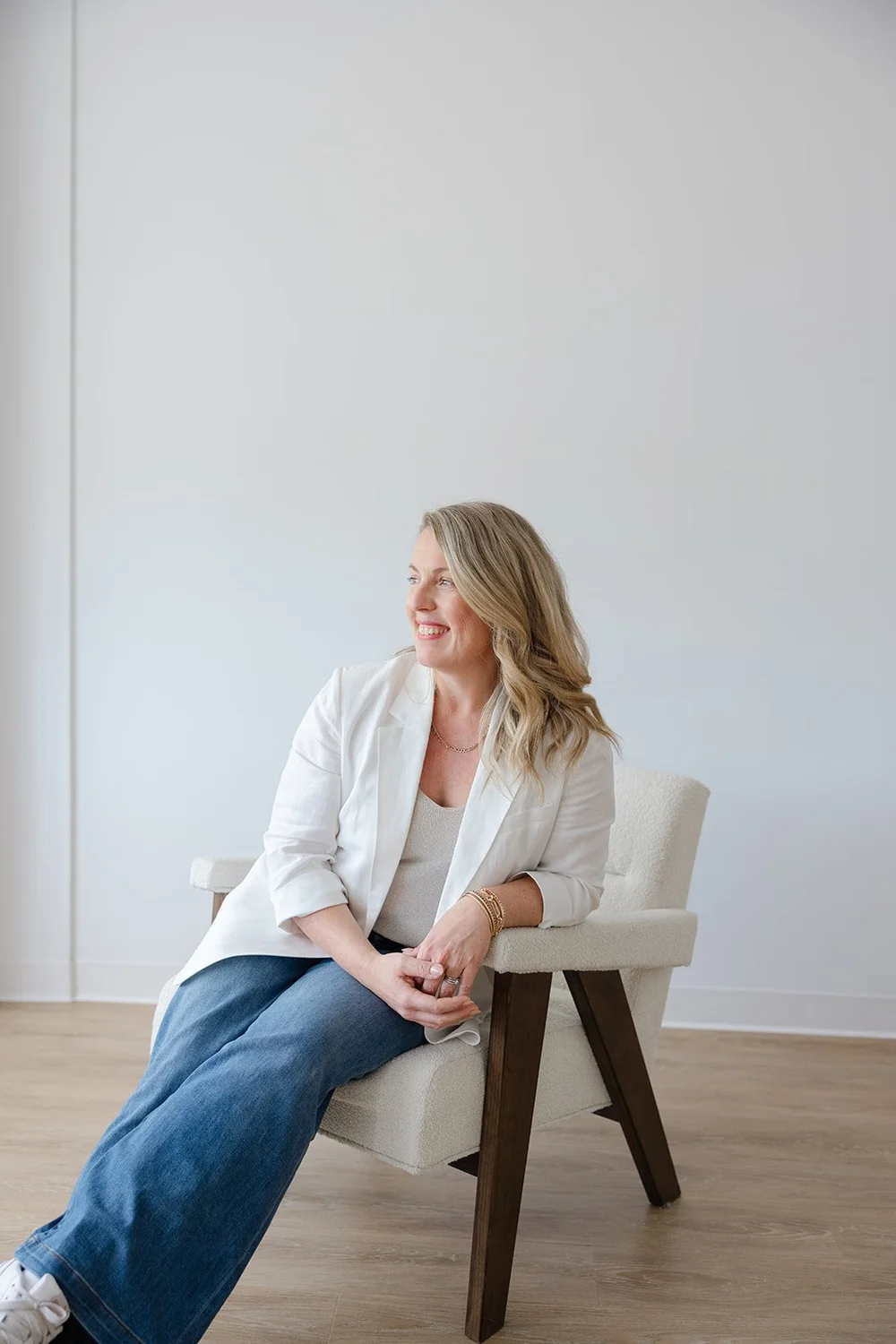 A woman in a white blazer seated in the accent chair by the window light
