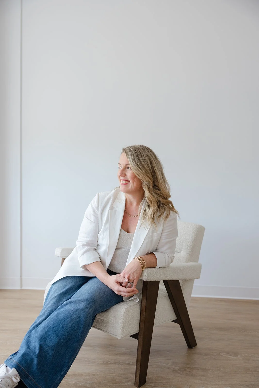 A woman in a white blazer seated in the accent chair, looking toward the window light