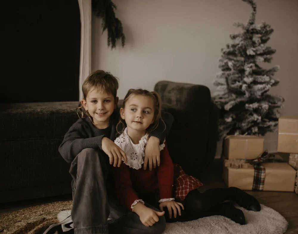 A brother and sister cuddled beside a flocked tree for a holiday mini session