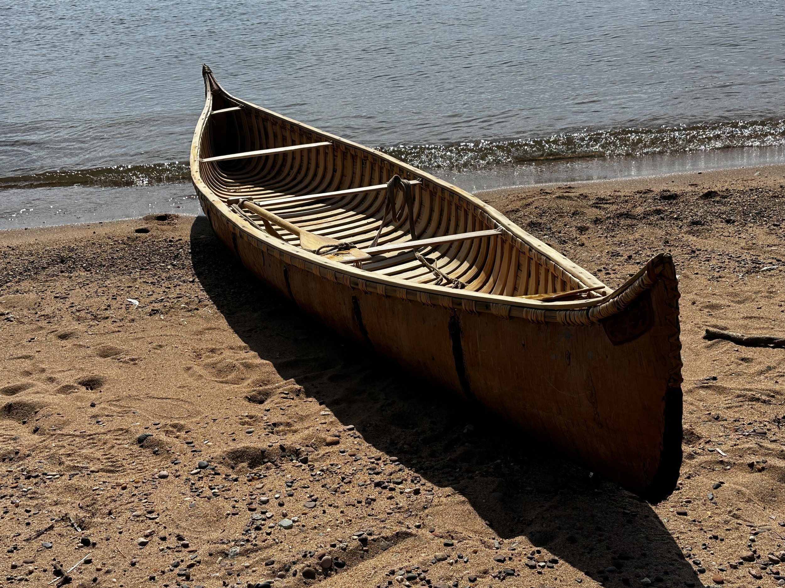 A traditional birch bark canoe resting on the Lake Superior shoreline