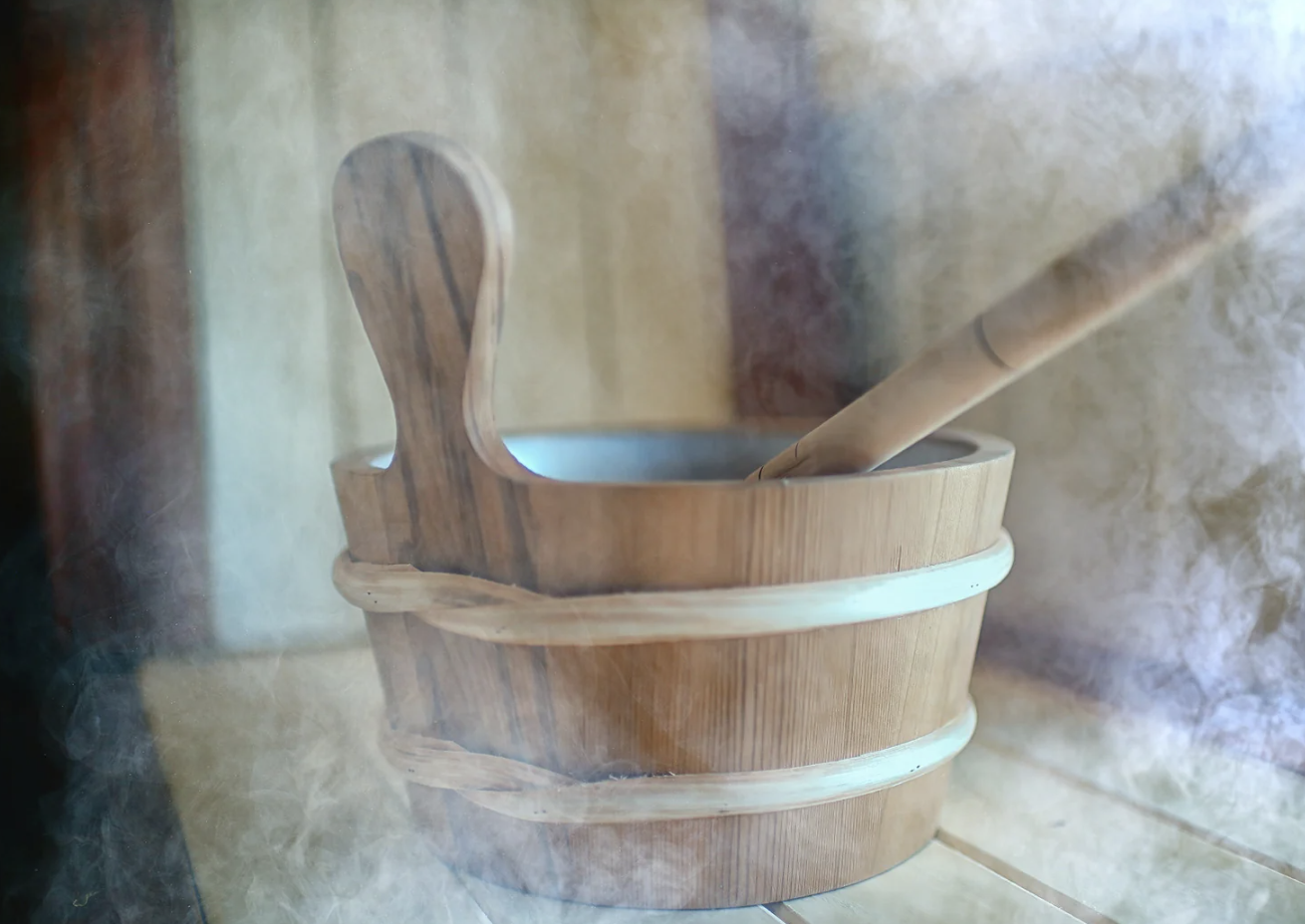 A wooden sauna bucket and ladle in steam