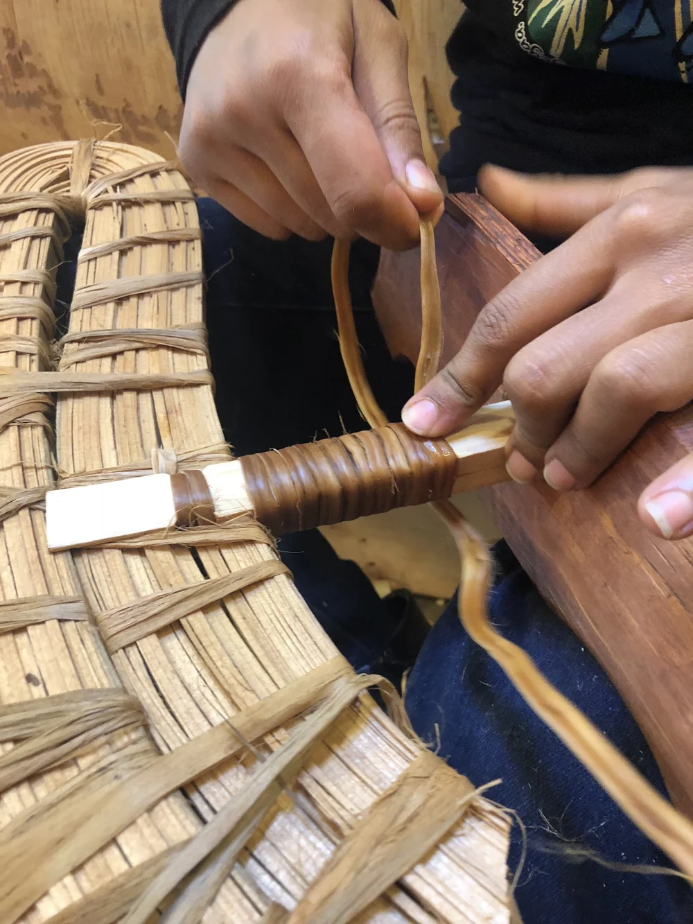 Hands binding the wooden framework of a birch bark canoe