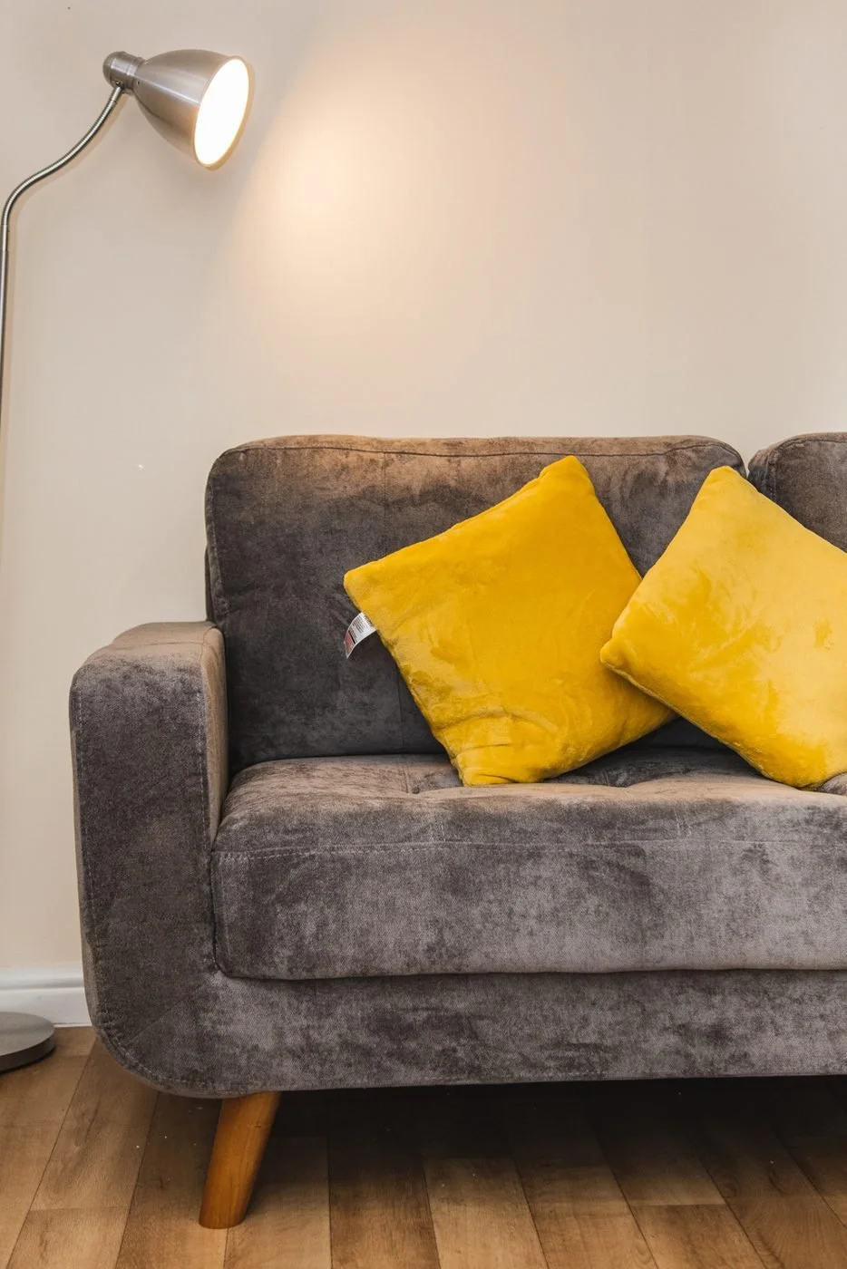 A grey sofa with yellow cushions beside a floor lamp