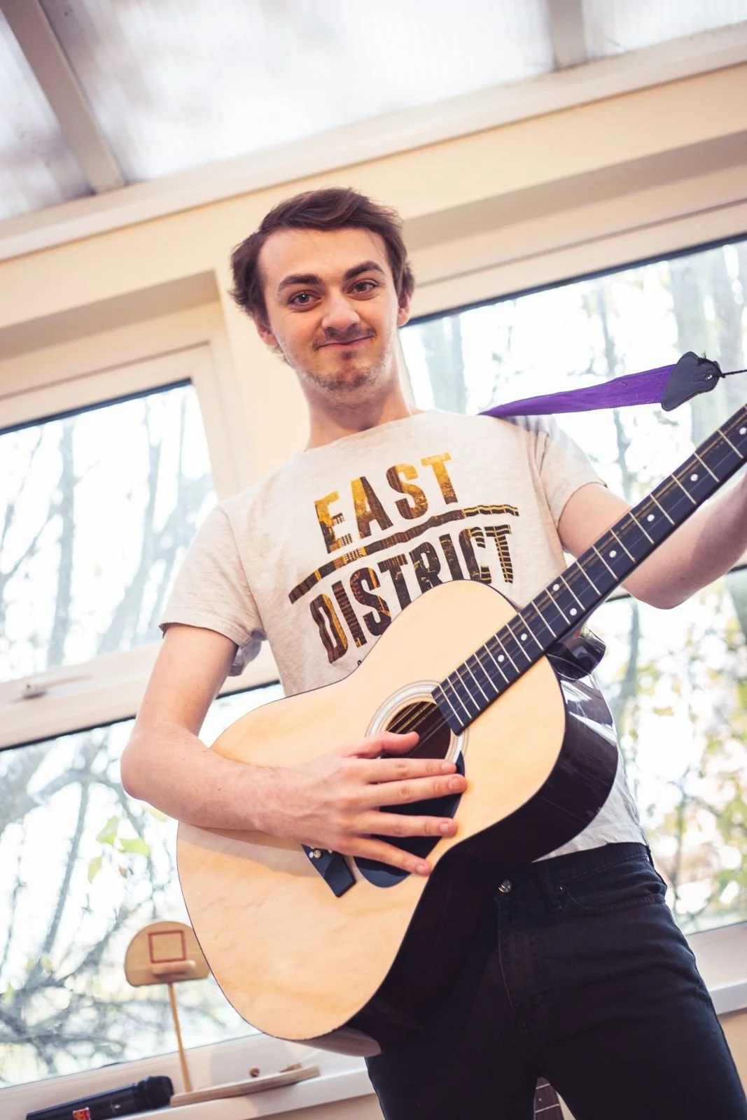 A young man smiling and holding an acoustic guitar