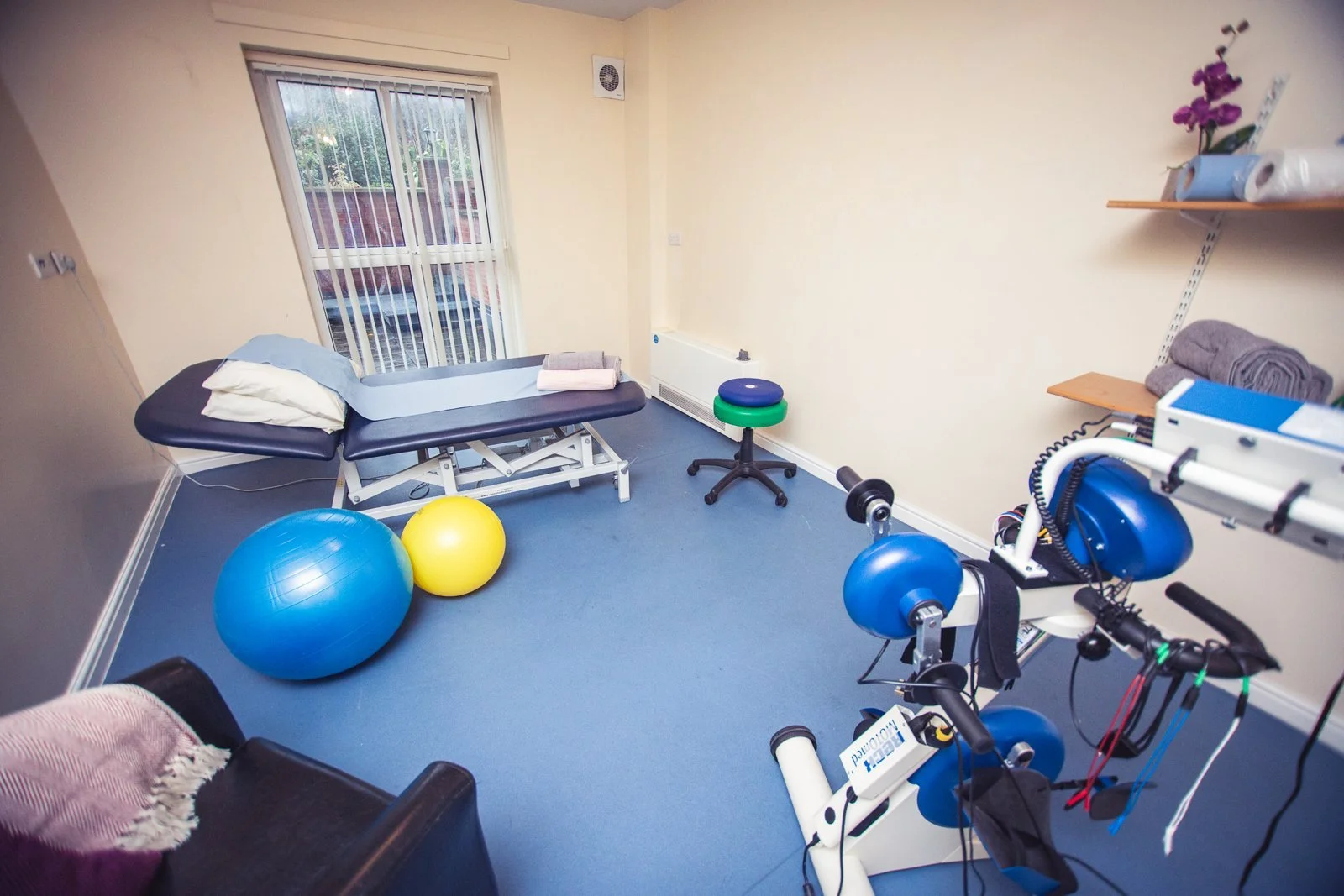 A therapy room with a treatment couch, exercise balls and a motorised exercise bike