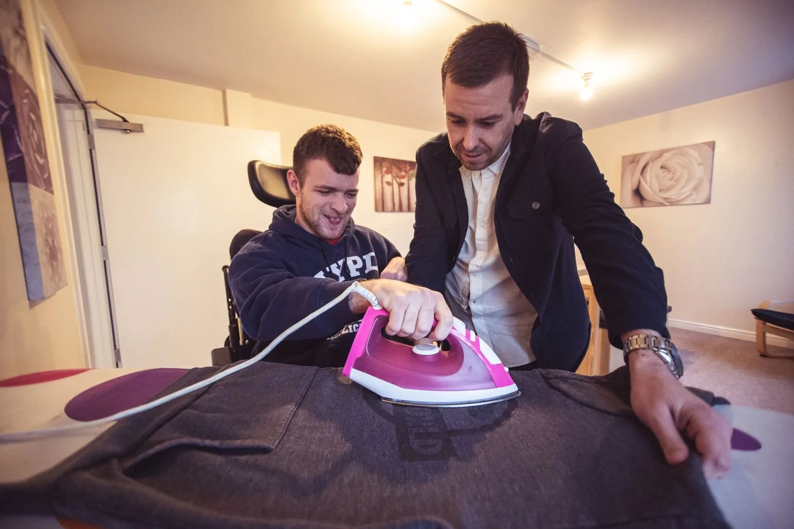 A support worker helping a young man in a wheelchair to iron a hoodie