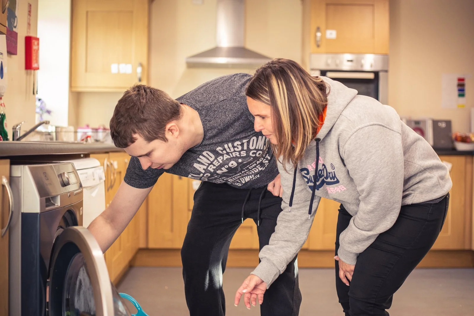 A support worker and a young man loading a washing machine together