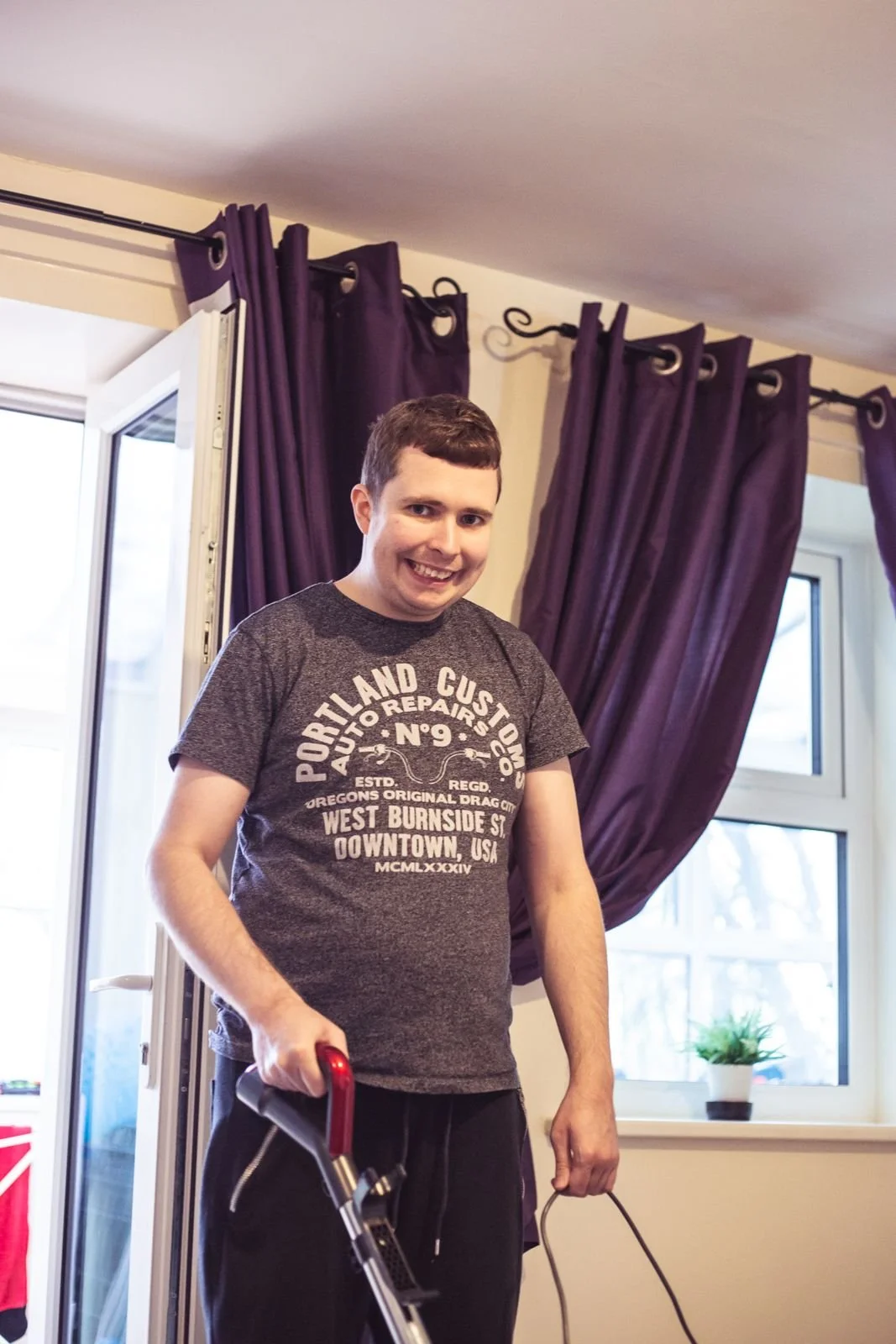 A young man smiling while vacuuming his living room