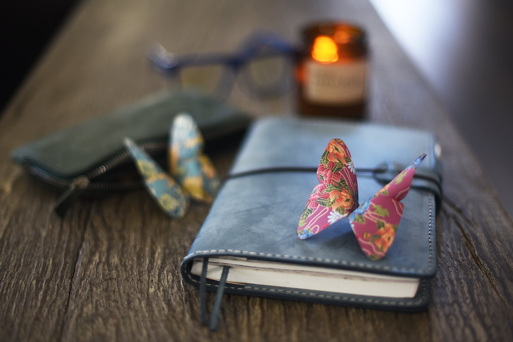 a leather-wrapped blue journal with pencil case, origami butterflies, a lit candle and caddis readers