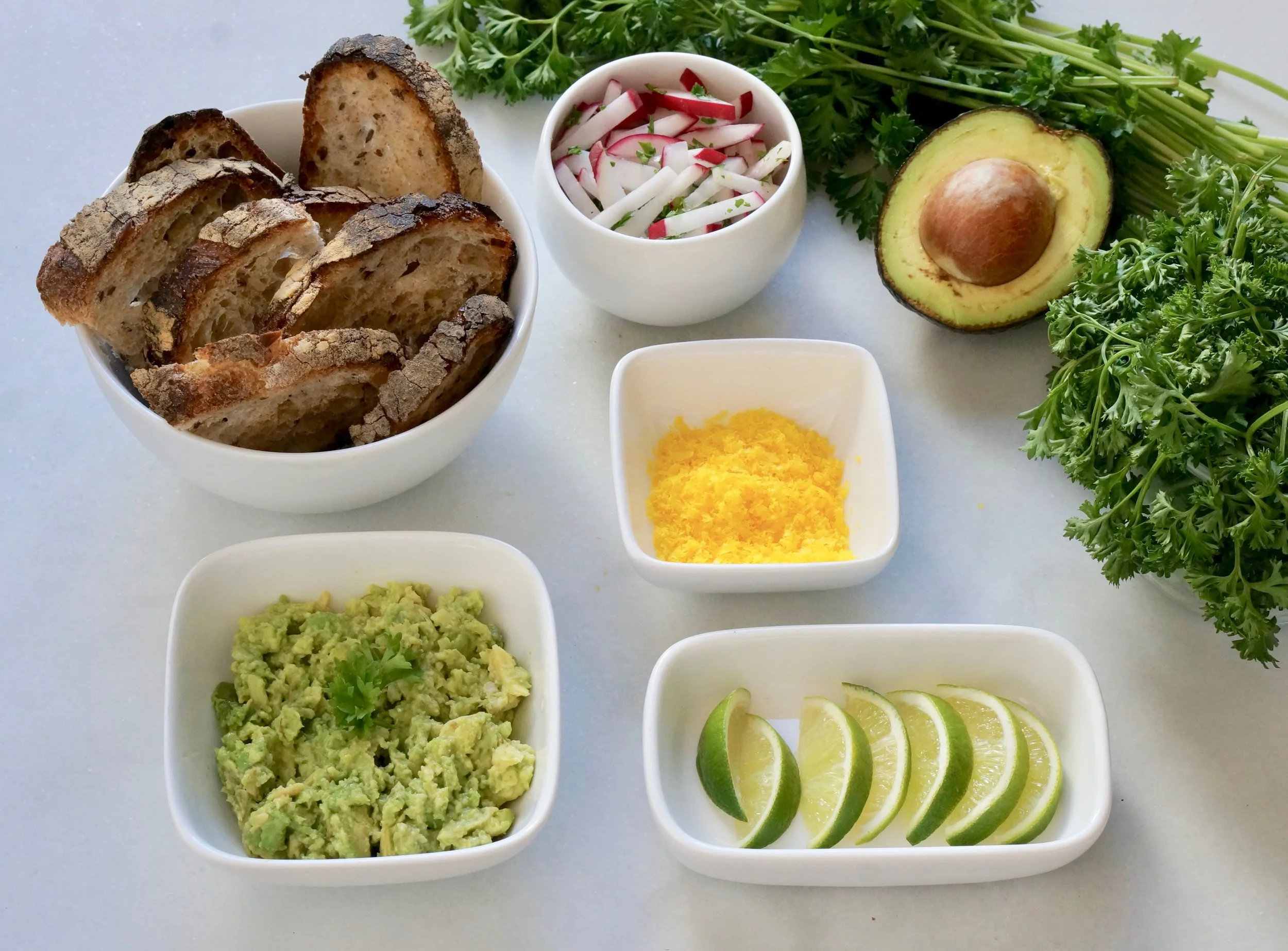 DIY Toast with cured egg shavings, guacamole, radishes and lime.