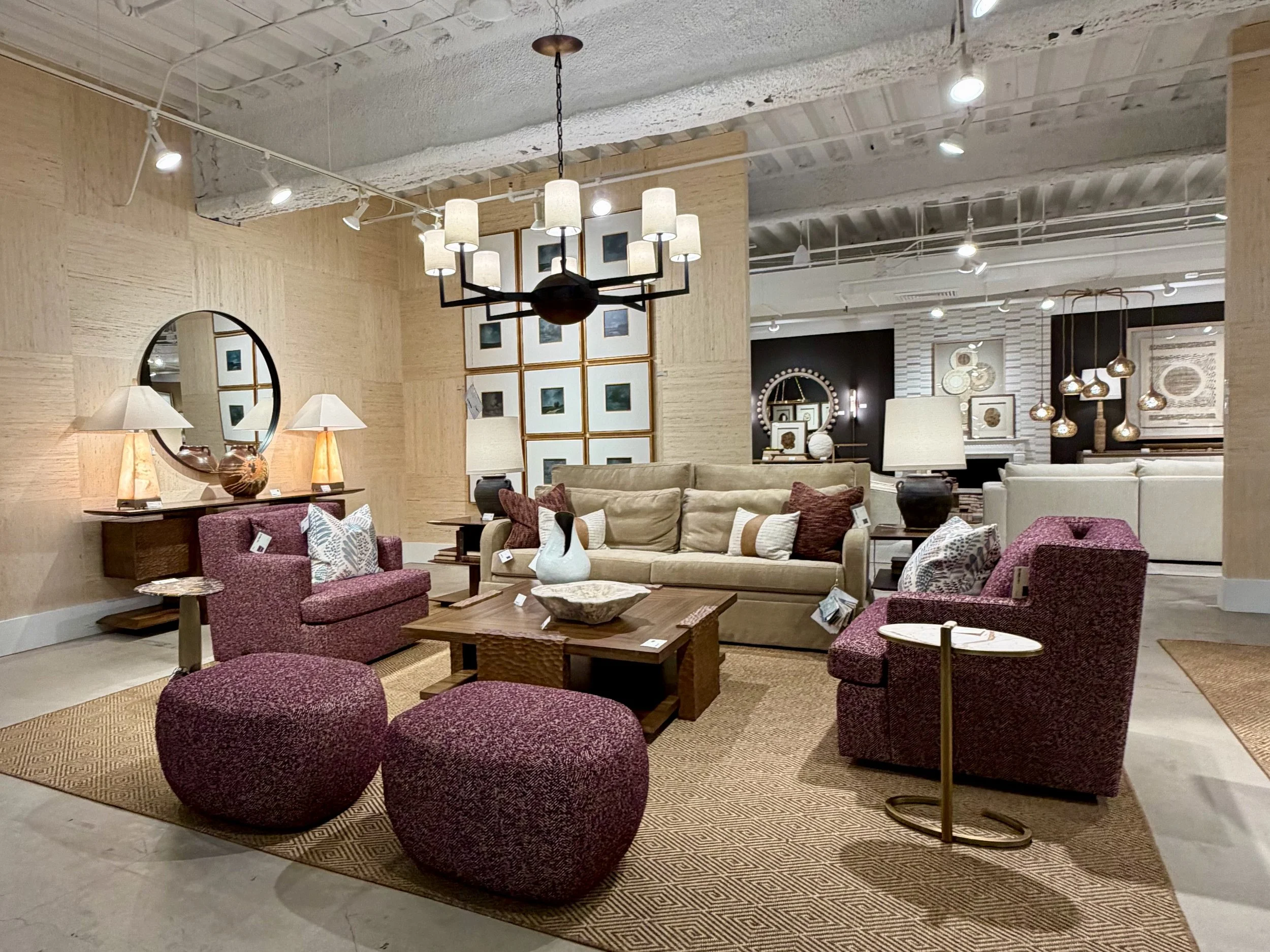 This image shows a living room setting in a showroom with a tan sofa, two plum colored arm chairs a coffee table and two matching plum colored ottomans.