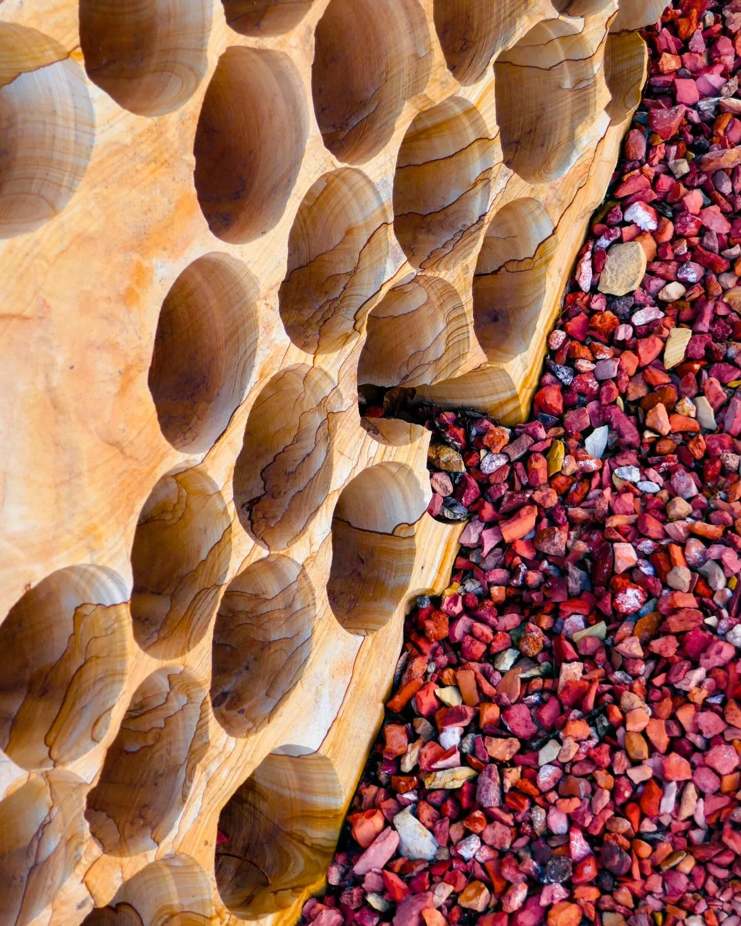 &ldquo;Honeycomb&rdquo; &copy; 2025 Skip Hunt

A stone surface with smooth, rounded indentations is juxtaposed against a bed of red and pink pebbles, creating a striking contrast between the natural grains of the wood and the vibrant stones. The patt