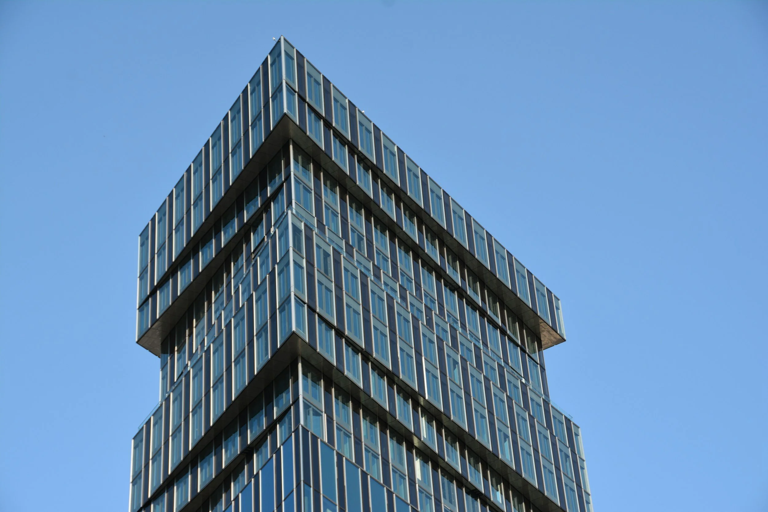 Modern glass office building with geometric design against a clear blue sky.
