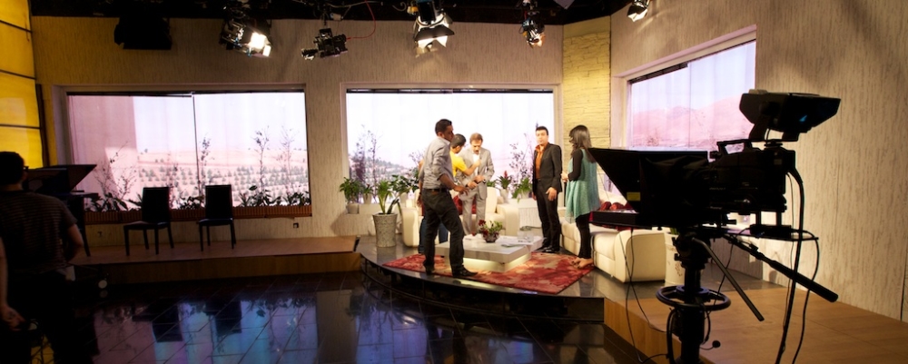 Television studio set with four people standing center, cameras, and crew preparing for filming.